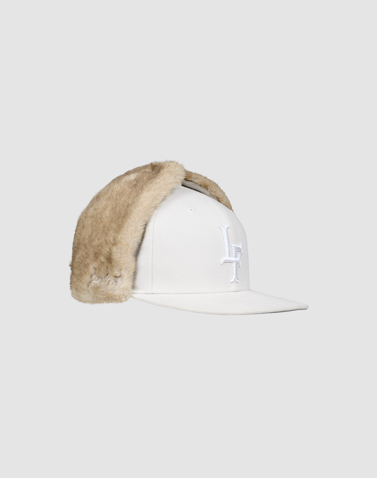 The LFDY x New Era 59Fifty DogEar by LIVE FAST DIE YOUNG is a white fitted cap with a flat brim, beige faux fur ear flaps, and a white LF logo on the front, shown against a plain gray background.
