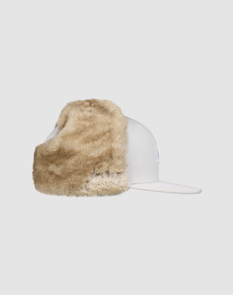 The LFDY x New Era 59Fifty DogEar by LIVE FAST DIE YOUNG, a white fitted cap with tan Kunstpelz ear flaps, is shown in a side view on a plain light gray background.