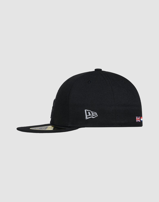 The LFDY X NEW ERA 59FIFTY Low Profile cap by LIVE FAST DIE YOUNG is black, shown side-on, with a white New Era logo, a small UK flag patch on the back, and a flat brim featuring a sticker underneath.