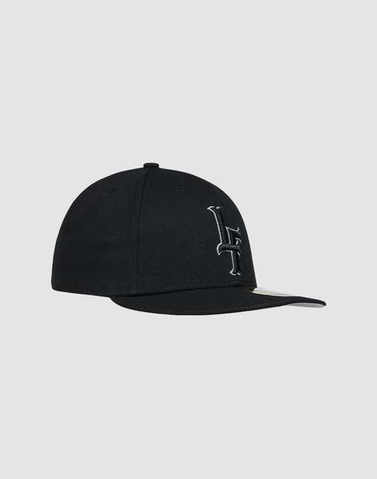 The LFDY X NEW ERA 59FIFTY Low Profile cap by LIVE FAST DIE YOUNG features a black design, curved brim, and a white embroidered L crossed by a line on the front, shown against a plain light gray background.
