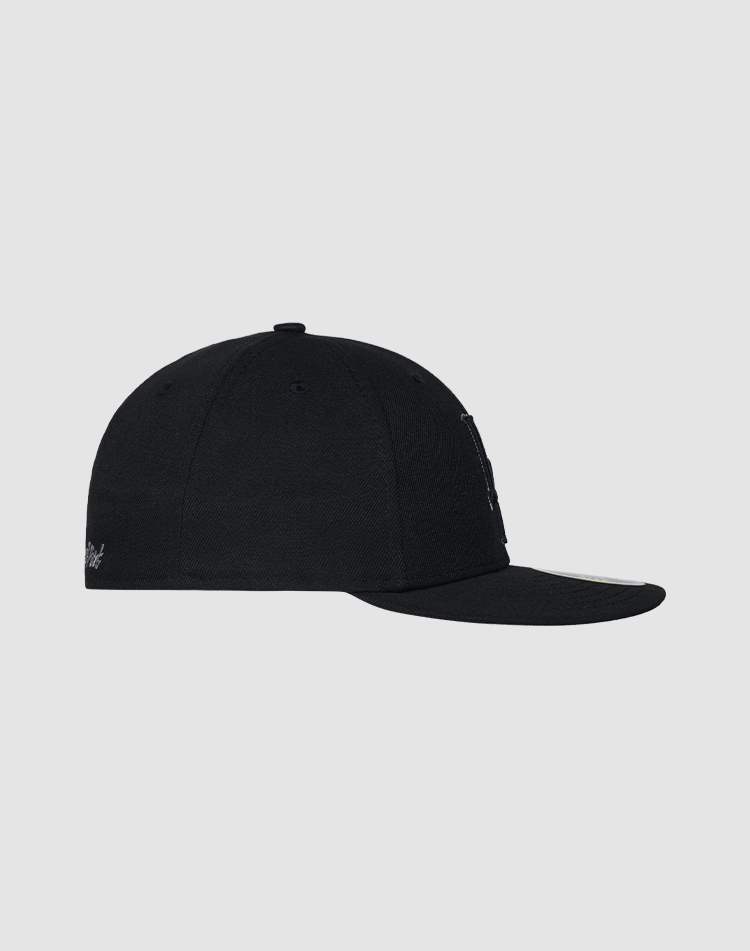 The LFDY X NEW ERA 59FIFTY Low Profile cap by LIVE FAST DIE YOUNG is shown in black from the side on a plain grey background, featuring a flat brim, visible stitching, and a small logo tag near the back.