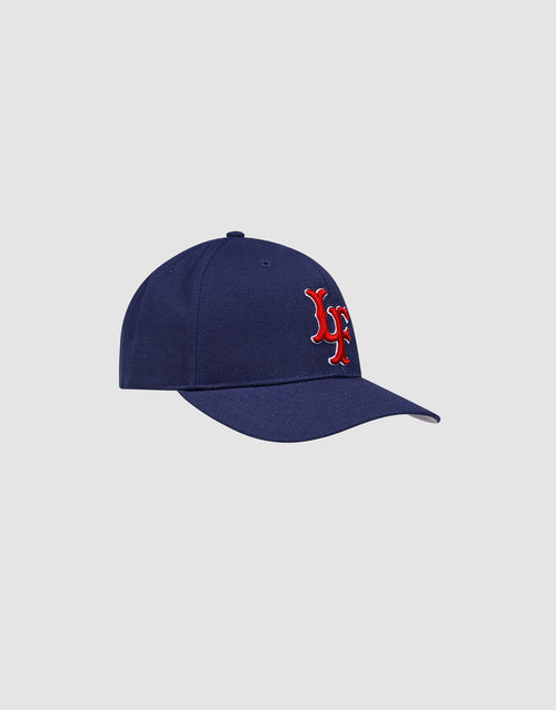 The LFDY Snapback by LIVE FAST DIE YOUNG features a navy blue design, red and white LF embroidery, Multi-Logo-Stick on the front, and snap closure. Model LF2605-20880. Displayed against a plain light gray background.