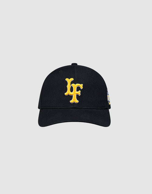 The LFDY Snapback by LIVE FAST DIE YOUNG is a black cap with a curved brim, green underside, large yellow LF initials on the front, a colorful patch on the left, and an adjustable snap closure. Shown on a plain light gray background. 