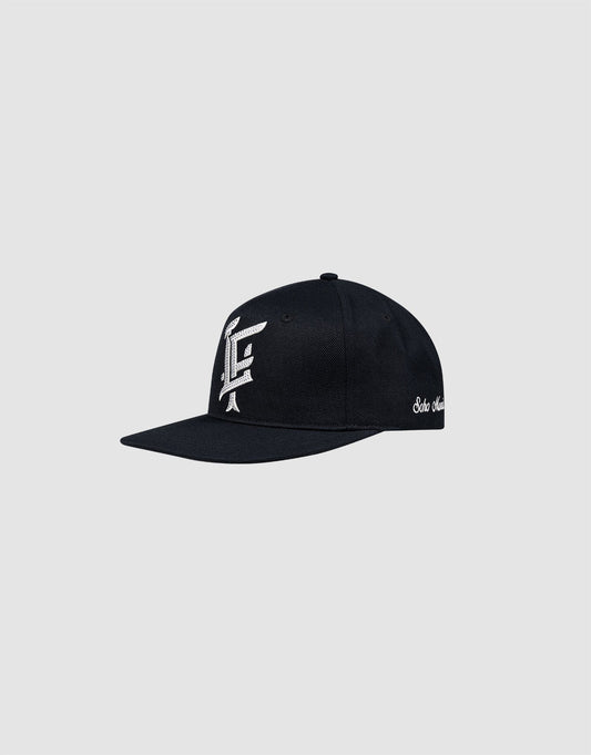 The LF Rhinestone Cap by LIVE FAST DIE YOUNG is a black cotton baseball cap with a flat brim, featuring a white logo embroidery on the front and white script on the side, shown on a plain light gray background.