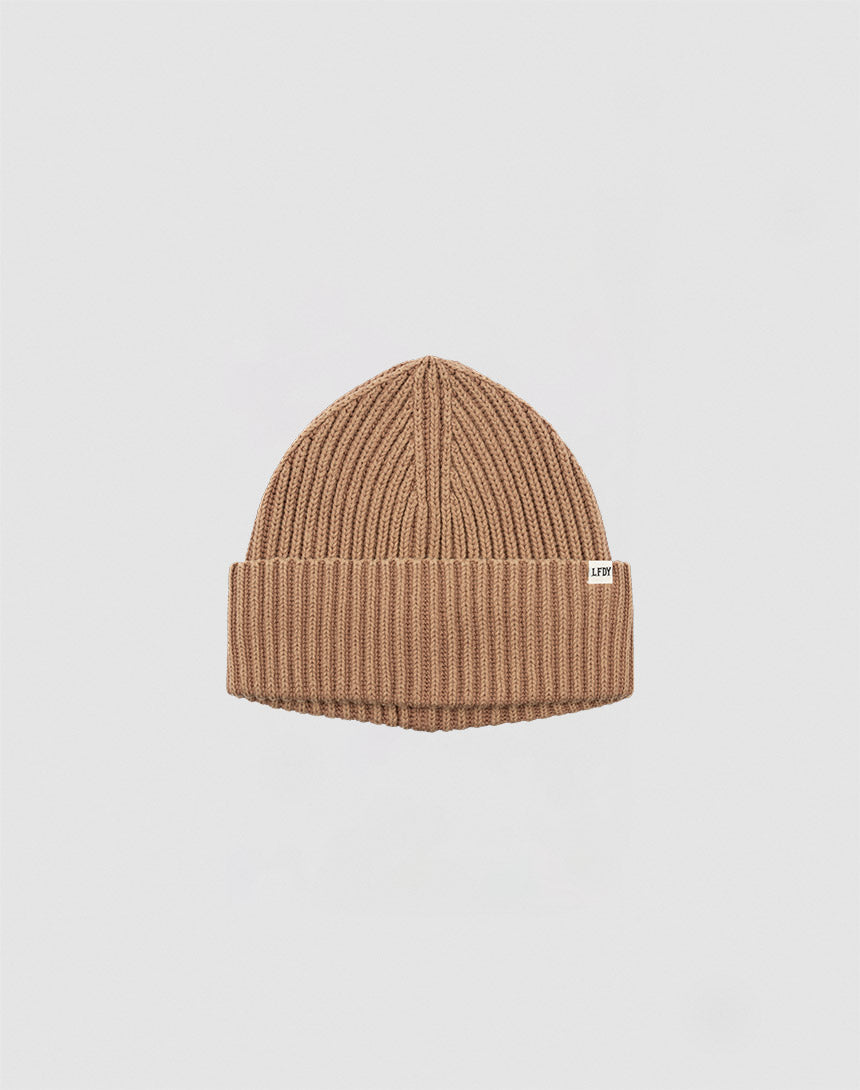 The LIVE FAST DIE YOUNG Rib Knit Beanie is tan, ribbed, one size, with a folded cuff and a small white flag label on the side, shown against a plain white background.