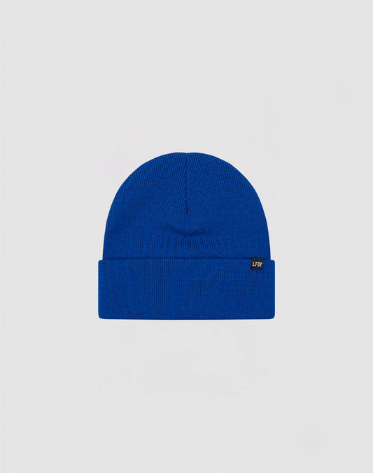 The LIVE FAST DIE YOUNG Basic Beanie is a plain royal blue polyacryl hat with a folded brim and a small black side flag label with white text, shown on a light gray background.