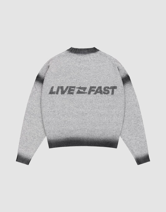 The LIVE FAST DIE YOUNG Live Fast Boucle Sweater features an oversize fit, gray tone, dark gradient cuffs, hem, and collar in a faded spray effect. "LIVE FAST" with a lightning bolt is printed bold on the back. Shown laid flat on a plain background.