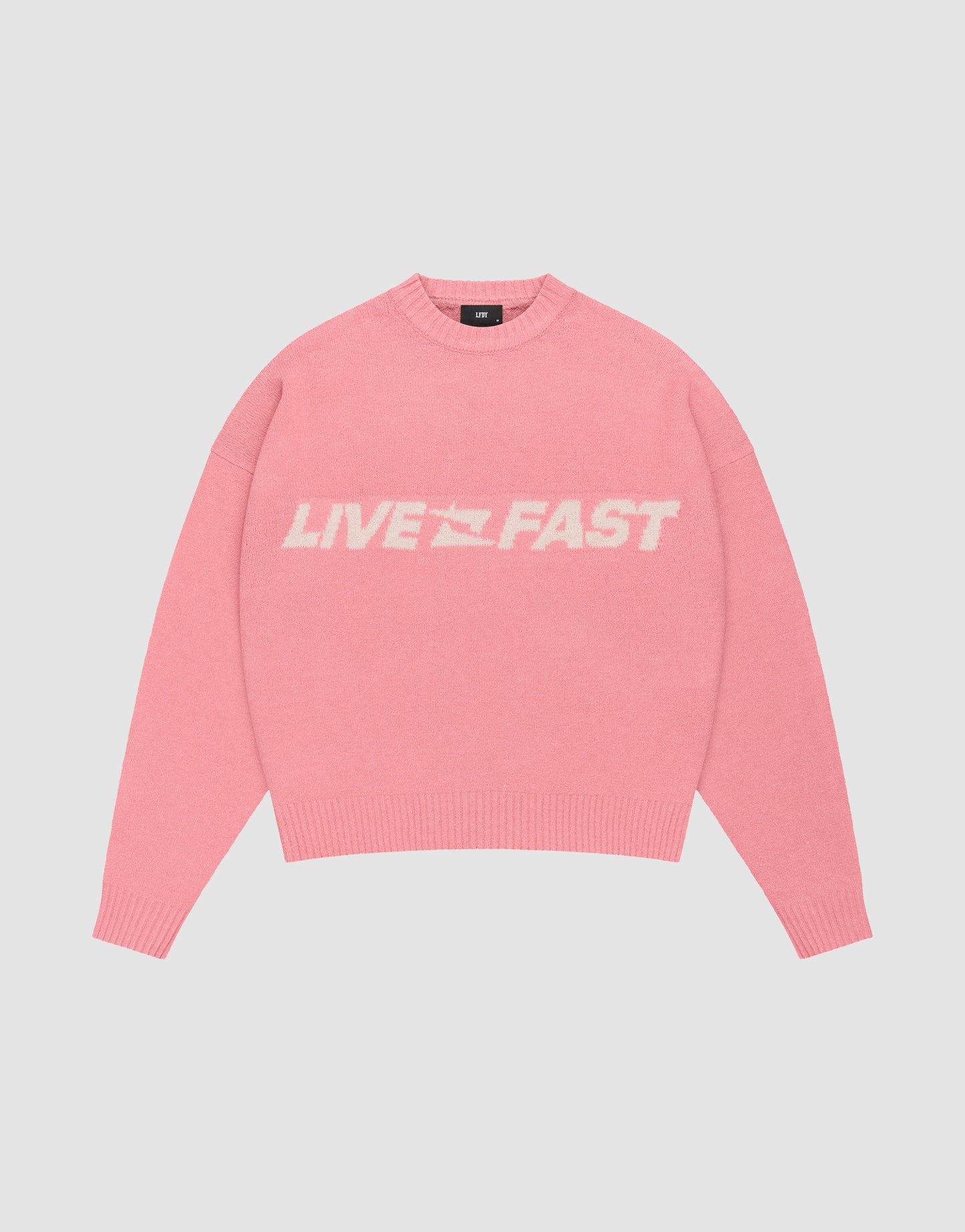 The Live Fast Boucle Sweater by LIVE FAST DIE YOUNG is a pink, oversized knit with bold white "LIVE FAST" lettering across the chest, shown against a plain light background.