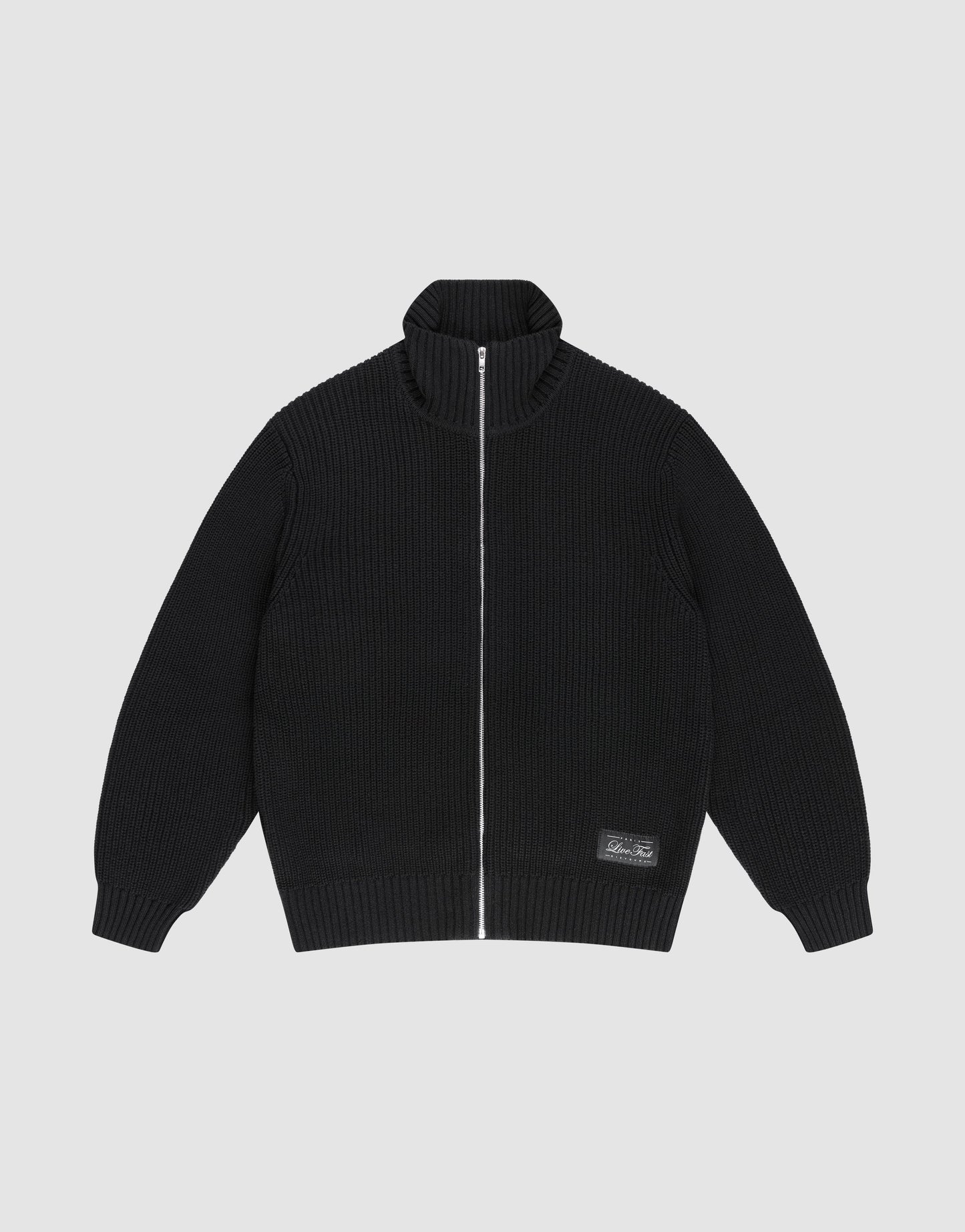 The LFDY Knit Jacket by LIVE FAST DIE YOUNG is a black, ribbed zip-up with Stehkragen, long sleeves, and a small rectangular patch near the hem. Made from 100% Baumwolle, it's shown laid flat on a light gray background. | plain