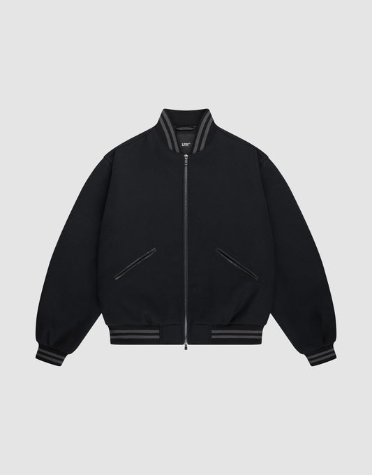 The LIVE FAST DIE YOUNG Live Fast College Jacket is a black varsity zip-up with a Metal Reißverschluss, ribbed gray-striped collar, cuffs, and hem, Logo Applikation on the chest, and two front diagonal zip pockets on a light gray background.