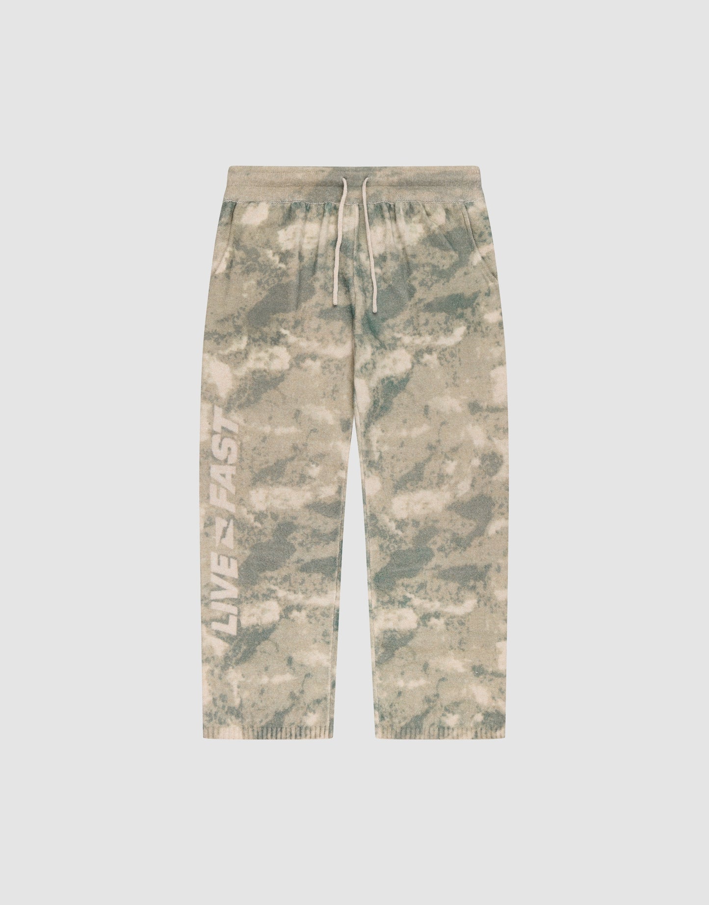 The LIVE FAST DIE YOUNG Live Fast Boucle Pants feature a beige and green tie-dye design, white drawstring, elastic waistband, "LIVE FAST" on the left leg, relaxed wide fit with straight leg and ribbed cuffs for comfort.