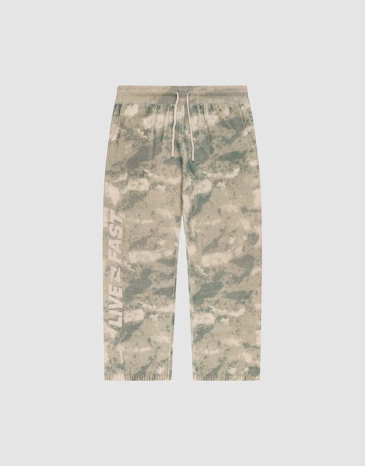 The LIVE FAST DIE YOUNG Live Fast Boucle Pants feature a beige and green tie-dye design, white drawstring, elastic waistband, "LIVE FAST" on the left leg, relaxed wide fit with straight leg and ribbed cuffs for comfort. | plain