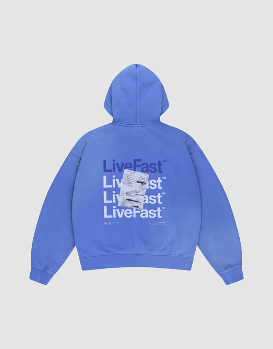 The Basic Evidence Hooded by LIVE FAST DIE YOUNG is a blue oversized hoodie with "LiveFast" printed repeatedly in bold white and purple on the back, topped with a sewn white rectangular patch. Shown laid flat on a white background. | plain
