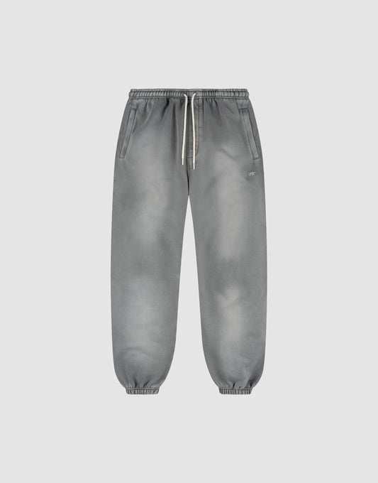 The LIVE FAST DIE YOUNG Basic Loose Jogger is a pair of gray washed sweatpants with a subtle fade effect, elastic waistband and white drawstring, side pockets, and elastic ankle cuffs, shown on a plain light background. | plain