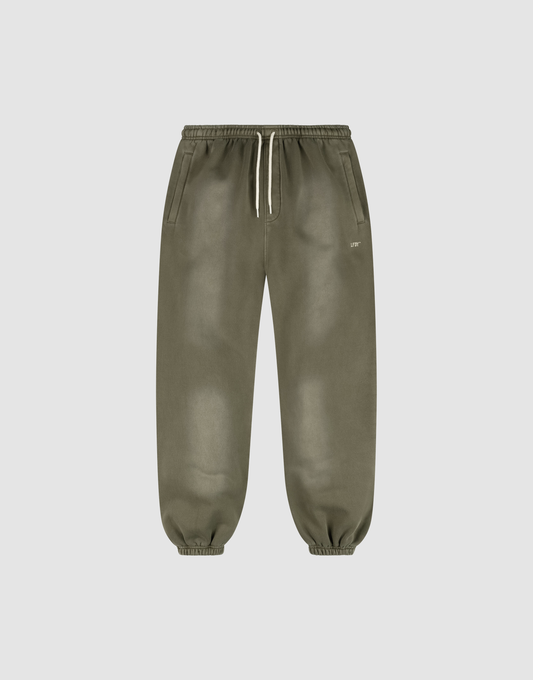 The LIVE FAST DIE YOUNG Basic Loose Jogger features olive green fabric with a handgefertigter Fade-Effekt, an elastic waistband with a white drawstring, side pockets, elastic ankle cuffs, and a small white logo near the left pocket. | plain