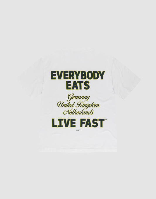 The Everybody Eats Tee by LIVE FAST DIE YOUNG is a white oversized cotton T-shirt with bold black and yellow front and back prints reading "EVERYBODY EAT$ Germany United Kingdom Netherlands LIVE FAST™," shown flat on a light gray background.