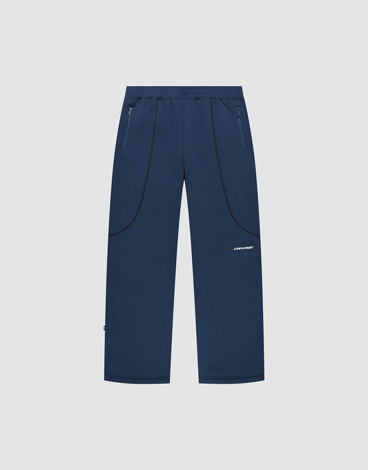 The LFDY Active Fleece Jogger by LIVE FAST DIE YOUNG features a navy blue wide fit, straight legs, zippered side pockets, black curved seam details, and a small white logo on the right thigh, shown on a light gray background. | plain