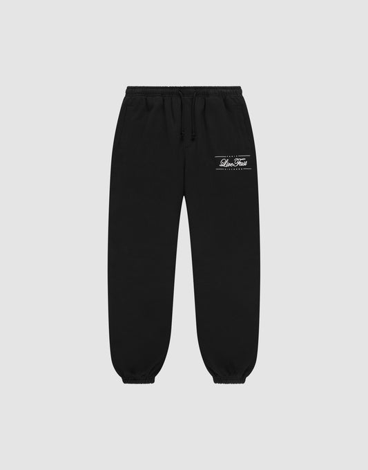 The LIVE FAST DIE YOUNG Wide Cuff Jogger is made from 100% Baumwolle French Terry, featuring an elastic waistband and cuffs with a white printed logo and text on the upper left thigh, shown on a plain light gray background. | plain