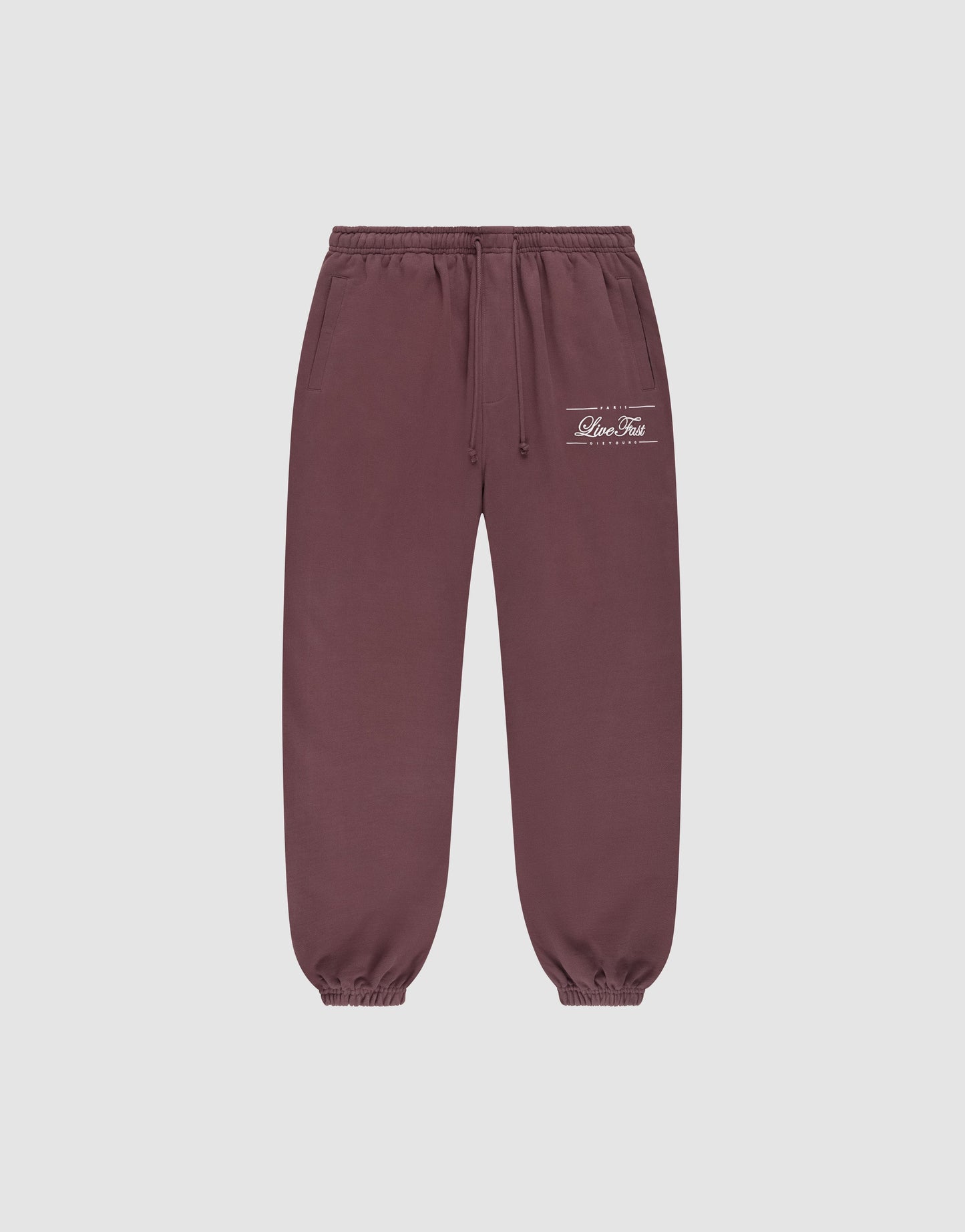 The LIVE FAST DIE YOUNG Wide Cuff Jogger in maroon is crafted from 100% cotton French Terry, featuring an elastic waistband, adjustable drawstrings, elastic cuffs, side pockets, and white text print on the left thigh. Background: light gray.