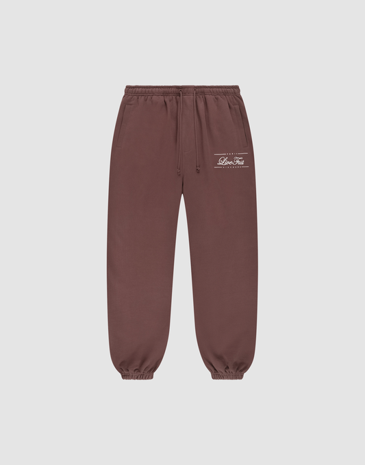 Die braune Wide Cuff Jogger von LIVE FAST DIE YOUNG aus French Terry hat Elastikbund, Seitentaschen, weiße Prints und Logo am linken Oberschenkel und ist vor grauem Hintergrund präsentiert. | plain