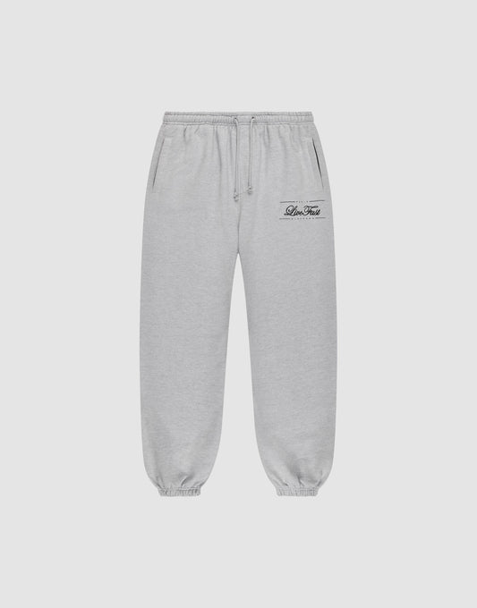 Light gray Wide Cuff Jogger sweatpants by LIVE FAST DIE YOUNG with a wide fit, elastic waistband with drawstring, side pockets, and elastic cuffs. Small black script logo on left thigh. Shown on a plain white background. | plain
