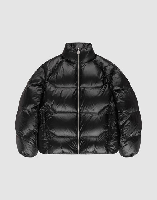 The LIVE FAST DIE YOUNG Live Fast Down Jacket is a shiny black oversized Daunenjacke with 600er Fillpower, high collar, front zipper, and quilted sections, shown against a plain light gray background. | plain