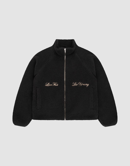 The LFDY Teddy Jacket by LIVE FAST DIE YOUNG is a black fleece jacket with raglan sleeves, side pockets, and gold "Live Fast" and "Die Young" embroidery on the chest, shown on a plain light gray background. | plain
