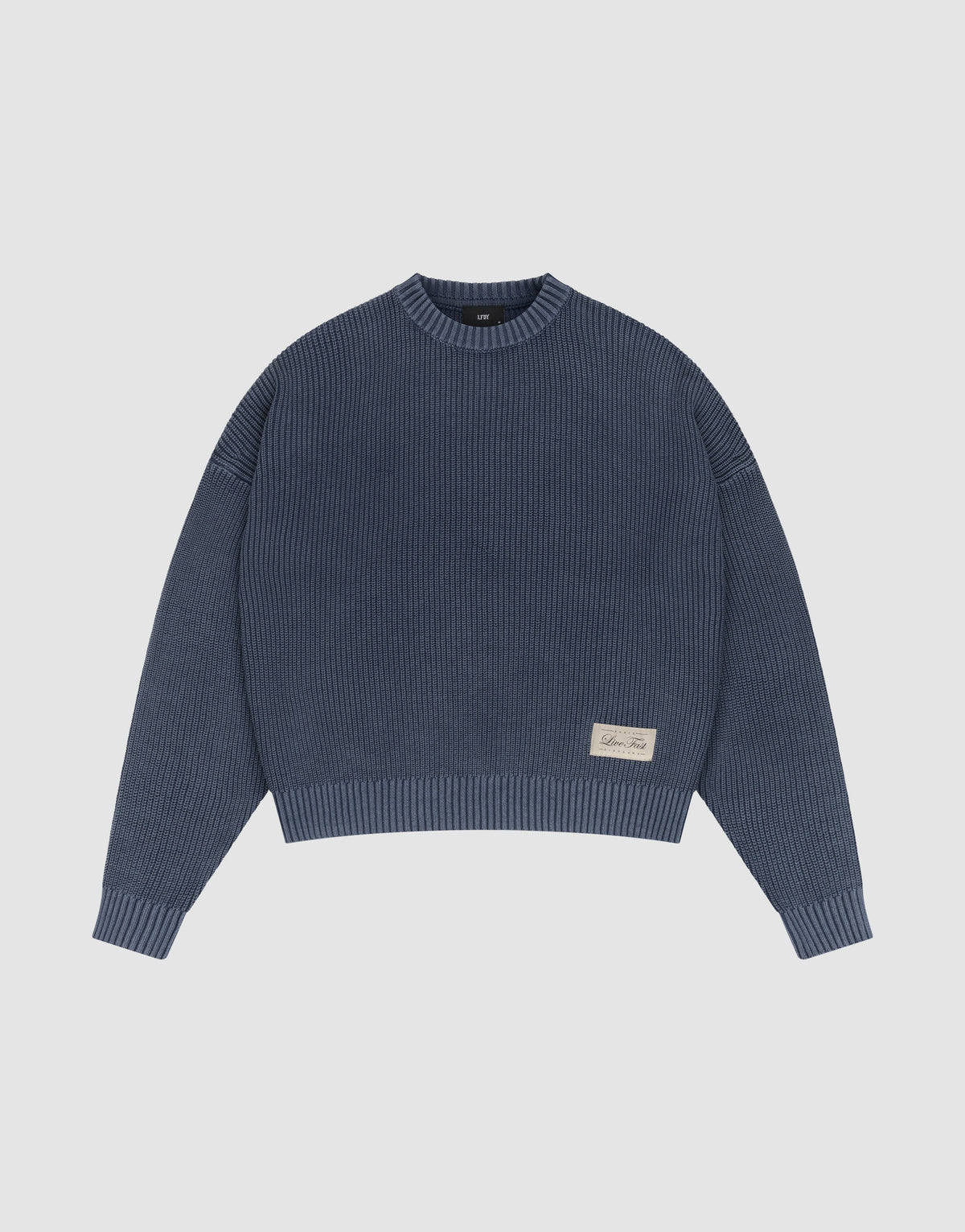 The LFDY Knit Sweater by LIVE FAST DIE YOUNG is a blue ribbed cotton piece with long sleeves, a crew neck, dropped shoulders, an oversized fit, and a beige tag near the hem. It’s shown laid flat on a plain white background.