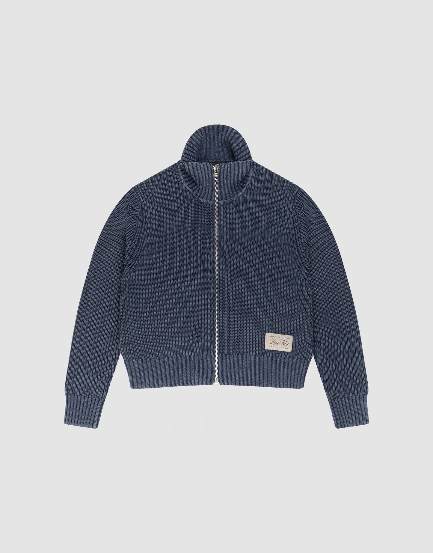 The LFDY Knit Jacket by LIVE FAST DIE YOUNG is a blue, regular-fit zip-up sweater with ribbed texture, high Stehkragen, long sleeves, and a white rectangular patch above the hem. It is displayed flat on a plain light background.