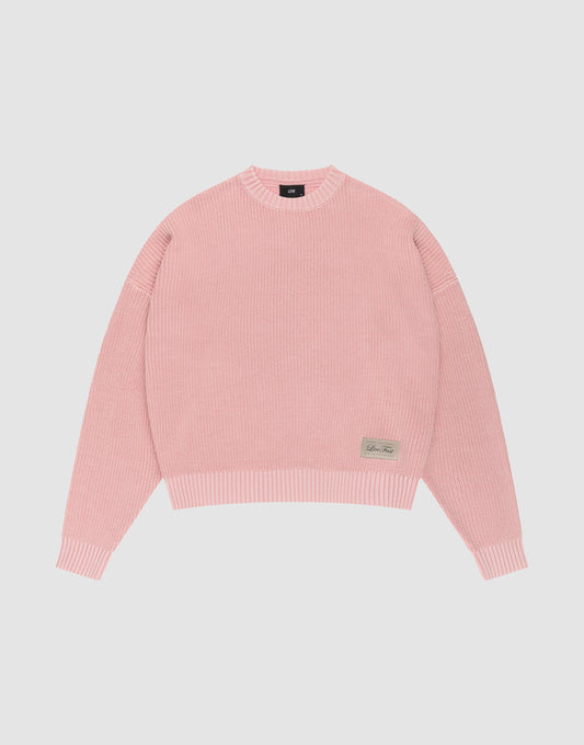 The LFDY Knit Sweater by LIVE FAST DIE YOUNG features pink ribbed knit, an oversized fit, dropped shoulders, long sleeves, a crew neckline, and a small rectangular beige patch with text on the front hem, displayed on a plain white background. | plain
