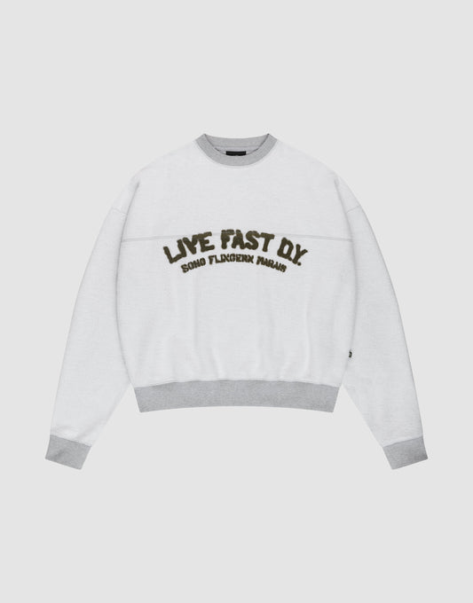 The LFDY District Sweater by LIVE FAST DIE YOUNG is a white oversized crewneck with light gray collar, cuffs, and hem in 480 GSM inside-out fabric. The chest displays bold LIVE FAST D.I.Y. text above ROAD FLECHTERIN PARADIS. | plain