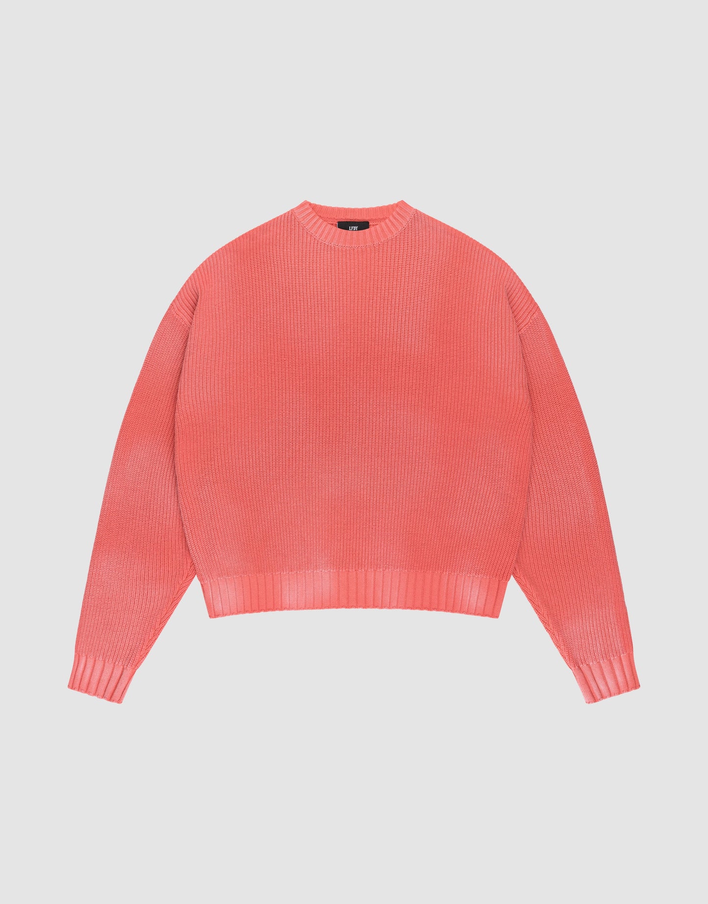 The LIVE FAST DIE YOUNG LFDY Washed Knit Sweater in coral pink features a crew neck, long sleeves, ribbed cuffs/collar/hem, and an oversize fit. Made from 100% Baumwolle, shown laid flat on a light gray background.
