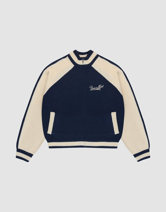 The LIVE FAST DIE YOUNG Boxy Knit Zip Jacket features a navy and cream varsity style with cream raglan sleeves, striped cuffs and collar, two front pockets, and Paradise embroidery on the left chest. Set against a plain light gray background.