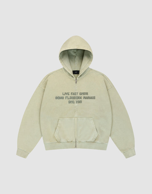 The LFDY District Hooded Zip by LIVE FAST DIE YOUNG is a light beige sweatshirt with front pockets, oversize fit, and subtle wash effect. Faded green chest text reads "LIVE FAST GMBH SOHO FLORIDE PARIAS RDC 225". Laid flat on white background. | plain