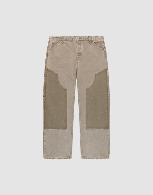 The LIVE FAST DIE YOUNG Faded Carpenter Pants are beige, straight-leg, baggy-fit jeans with large darker beige patches on the front thigh and knee, featuring front pockets and belt loops, displayed flat on a light background. | plain