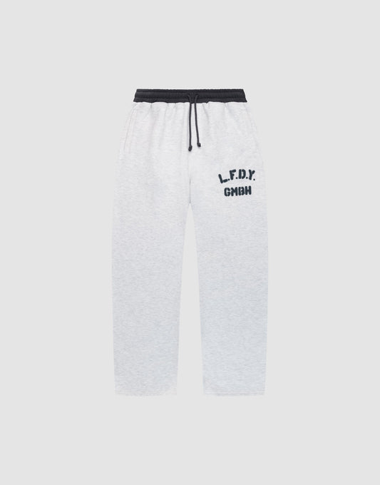 The LFDY District Jogger by LIVE FAST DIE YOUNG features a wide fit in light gray, black elastic waistband with drawstring, black "L.F.D.Y." and "GMHN" prints on the left thigh, plus zip pockets. Displayed on a plain light background. | plain