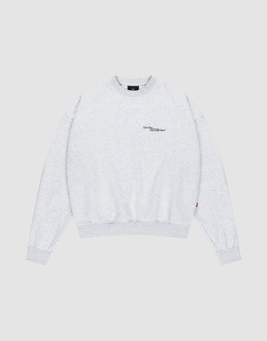 The LFDY SiXXXth Store Sweater by LIVE FAST DIE YOUNG is a light gray, oversized crewneck made from soft cotton. It features long sleeves, ribbed cuffs and hem, and a subtle black logo on the left chest. Plain light gray background.