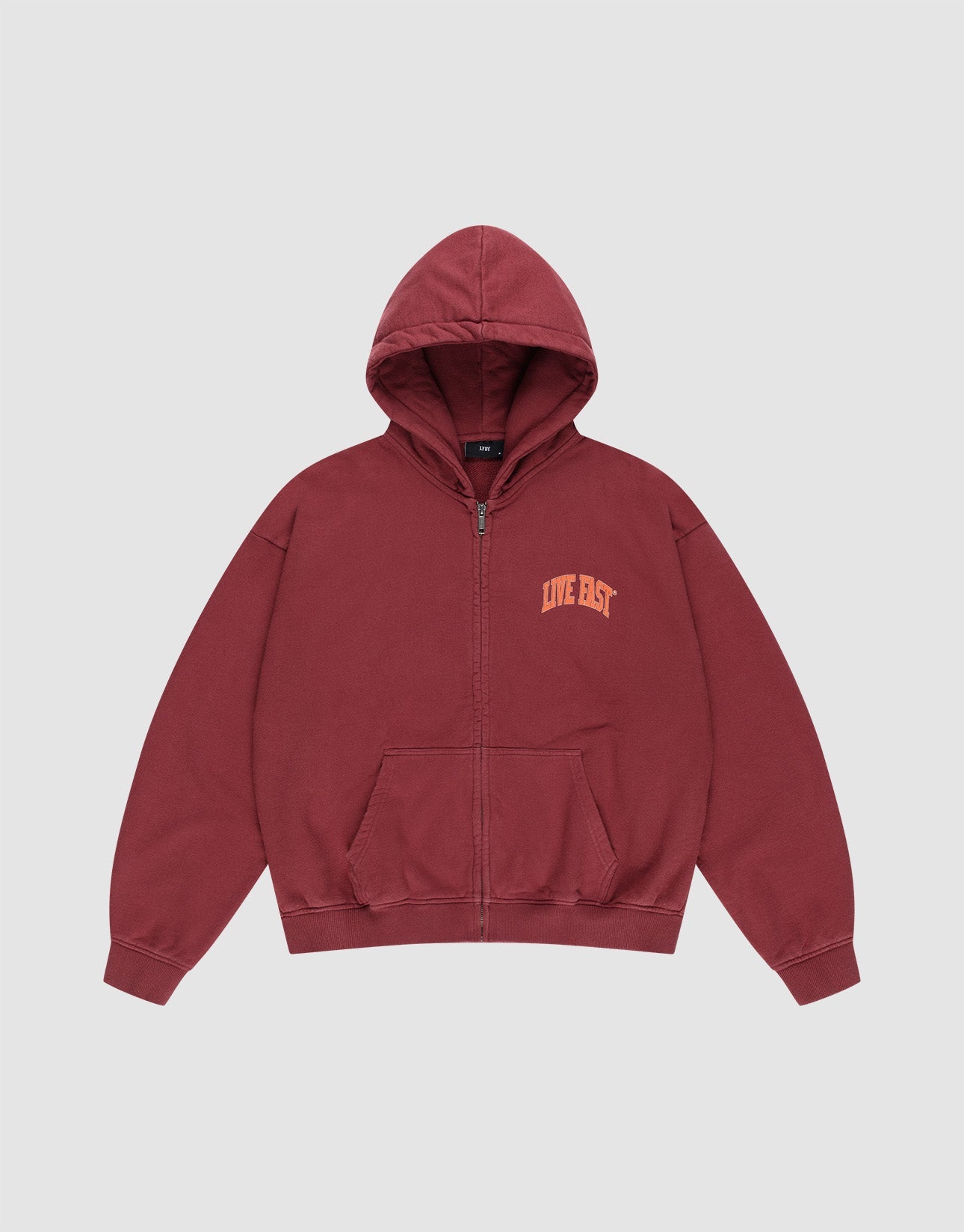 A man stands against a plain background wearing the LIVE FAST DIE YOUNG “Live Fast London Hooded Zip” and matching maroon sweatpants with yellow front and back prints, made from 100% cotton, hands in pockets, styled with white sneakers.