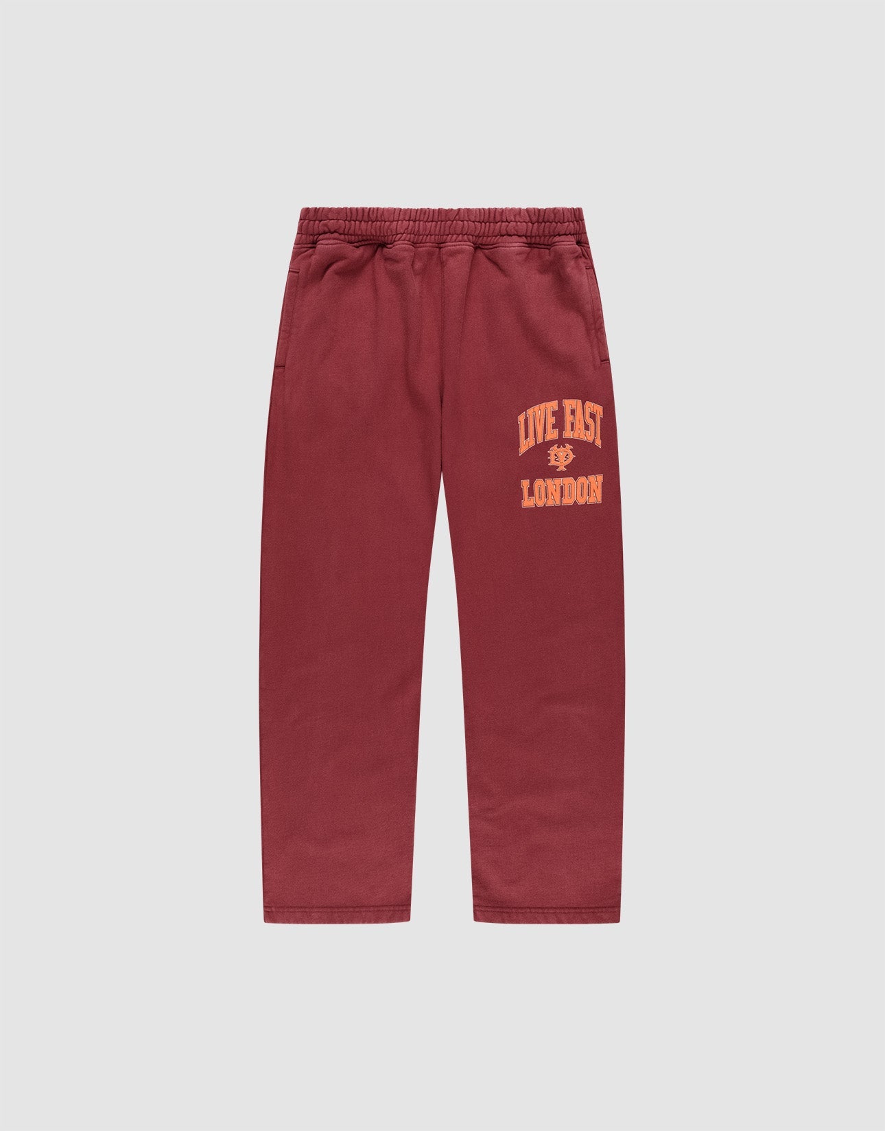 The LIVE FAST DIE YOUNG Live Fast London Wide Jogger in maroon, made from cotton, features a wide elastic waistband, side pockets, and "LIVE FAST LONDON" in yellow on the left thigh. Pants shown laid flat on a light gray background.