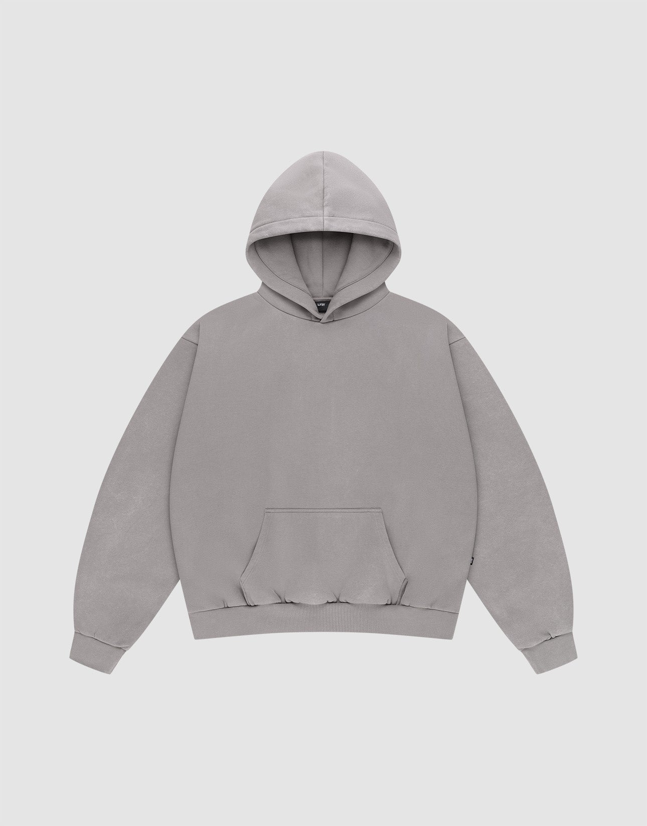 A person with short, twisted hair wears a loose-fitting gray LIVE FAST DIE YOUNG Basic Blank Hooded in Oversize Fit and olive green pants, standing against a plain light gray background.