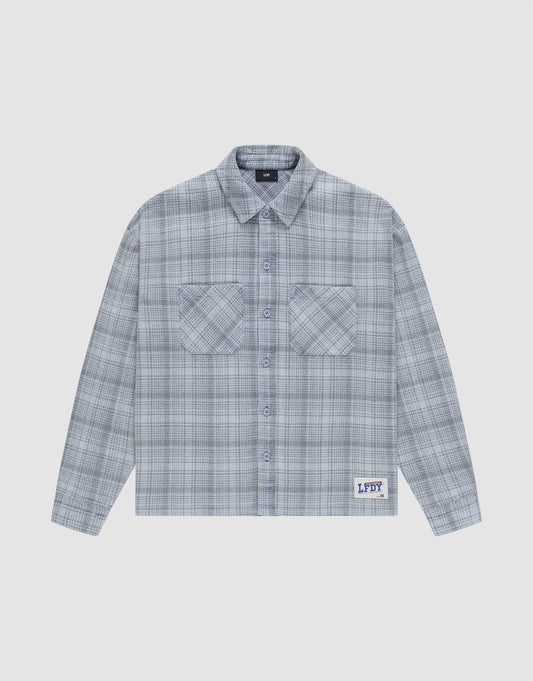 The Vintage Flannel by LIVE FAST DIE YOUNG is a gray plaid, long-sleeve, button-up shirt with two chest pockets and a small LFDY patch near the hem, featuring an oversize fit and vintage wash, shown laid flat on a white background. | plain
