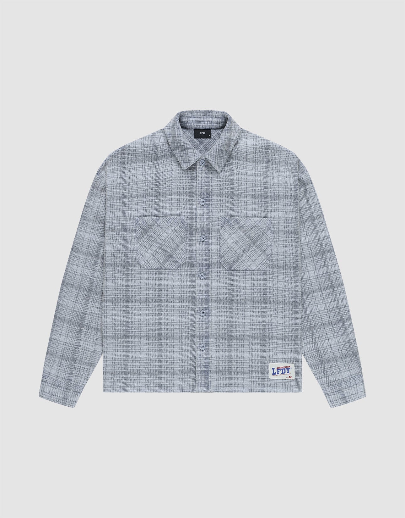 The Vintage Flannel by LIVE FAST DIE YOUNG is a gray plaid, long-sleeve, button-up shirt with two chest pockets and a small LFDY patch near the hem, featuring an oversize fit and vintage wash, shown laid flat on a white background.