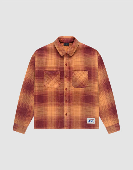 The LIVE FAST DIE YOUNG Vintage Flannel is a long-sleeve, button-up shirt with an oversized fit, red and orange plaid pattern, two chest pockets, and a blue brand patch near the hem, shown on a plain light background. | plain
