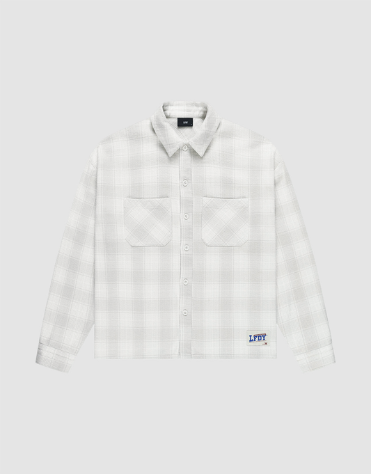 The LIVE FAST DIE YOUNG Vintage Flannel is a white plaid oversize long-sleeve shirt with two chest pockets, vintage wash, and a blue logo patch above the hem on a light grey background. | plain