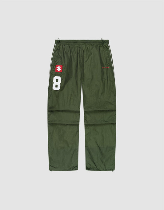 The LFDY Nylon Trackpants by LIVE FAST DIE YOUNG feature an olive green polyamide wide fit, a white number 8 and red-and-white logo patch on the left thigh, plus a small red logo on the right thigh, shown on a plain light background. | plain