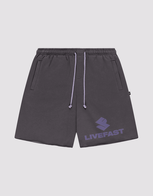 The LIVE FAST DIE YOUNG Live Fast LF Shorts are dark gray, wide fit athletic shorts featuring an elastic waistband, lavender drawstrings, side pockets, and a bold lavender LIVEFAST logo with emblem on the left leg. | plain