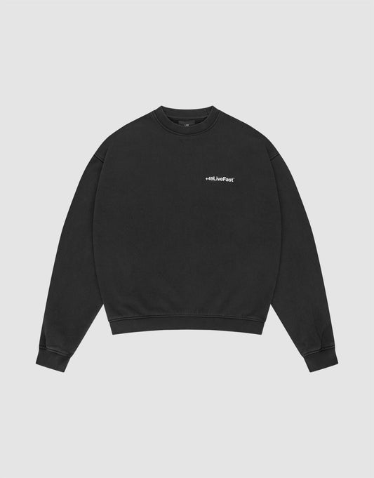 The LIVE FAST DIE YOUNG Basic +49 Chest Sweater is a black, oversized crewneck with ribbed cuffs and a small white #LLJLiveFast chest print, made from a cotton-polyester blend, shown flat on a light gray background. | plain