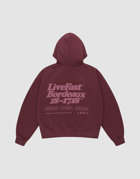 The LIVE FAST DIE YOUNG Basic 360 Hooded is a maroon oversized cotton hoodie with a hood, front and back prints including a large light purple "LiveFast Bordeaux 18-1718" text and small symbols on the back. | plain