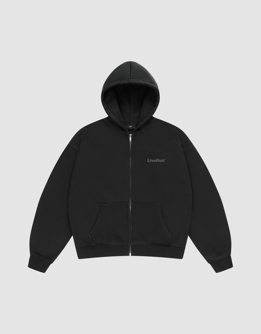 The BASIC 510 HOODED ZIP by LIVE FAST DIE YOUNG is an oversize fit black zip-up hoodie with a hood and front pockets, shown on a light gray background. “LiveFast” is subtly printed on the left chest.