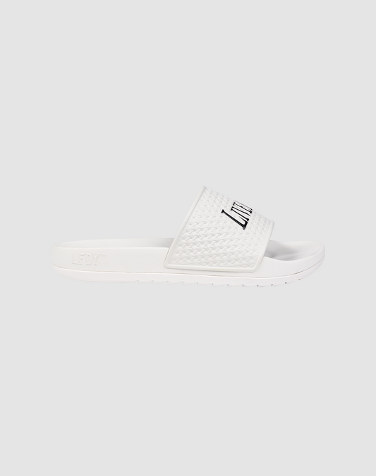 The LFDY Slides by LIVE FAST DIE YOUNG feature a white slip-on design with a textured PU strap, "LFTY" in black, and a comfy EVA sole. Shown on a light gray background. Style code: LF2606-20682.